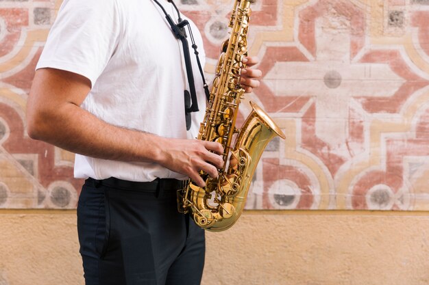 Plano americano de hombre de perfil tocando el saxofón sobre fondo geométrico