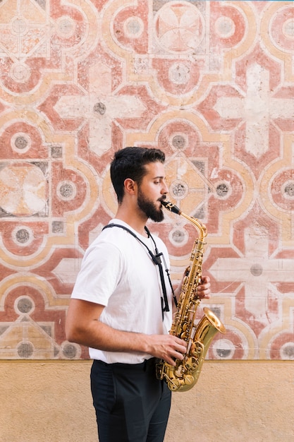 Plano americano de hombre de perfil tocando el saxofón sobre fondo geométrico