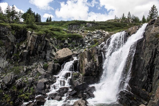 Plano amplio de una cascada desde un acantilado con césped y árboles en la superficie en un día nublado