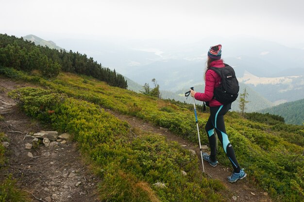 Plano amplio de una mujer subiendo una montaña con equipo completo en un clima frío y brumoso