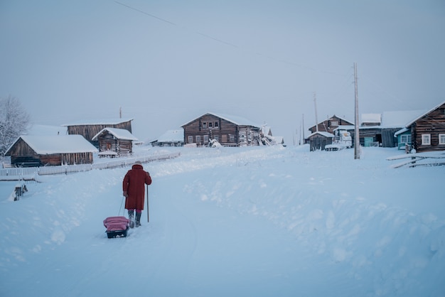 Plano amplio de un pueblo y una persona con un abrigo rojo caminando por la espesa nieve en un día frío