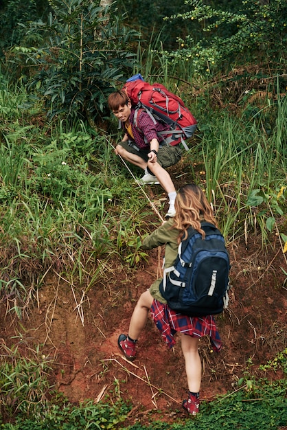 Plano completo de excursionista masculino que extiende una mano amiga a una excursionista femenina que intenta montar una colina