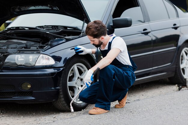 Plano completo del hombre agachado junto al auto