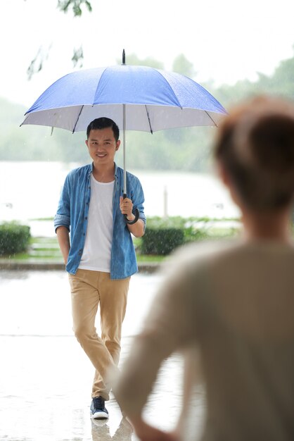 Plano completo del hombre de pie con paraguas bajo la lluvia esperando su cita