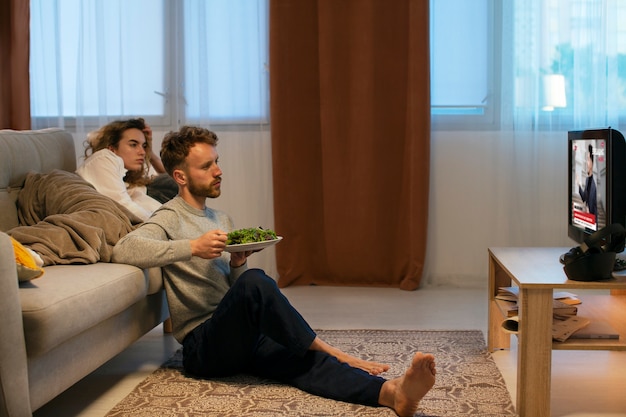 Plano completo de personas comiendo y viendo tv.