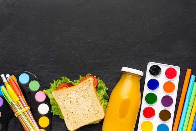Foto gratuita plano de elementos esenciales de la escuela con sándwich y jugo