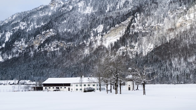 Plano general de una casa blanca rodeada de árboles y montañas cubiertas de nieve