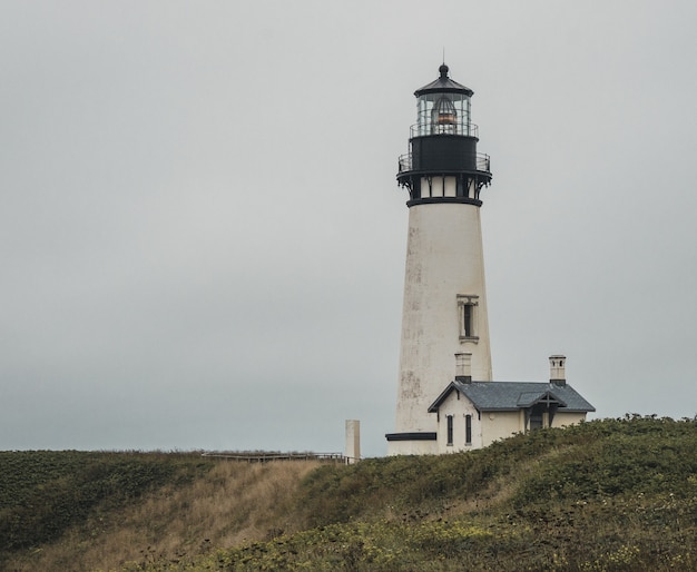 Foto gratuita plano general de un faro blanco y negro cerca de una casa en la cima de una colina