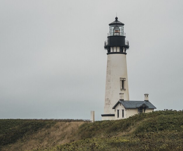 Plano general de un faro blanco y negro cerca de una casa en la cima de una colina