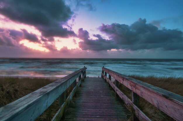 Plano general de un malecón que conduce a una playa con un colorido atardecer en Wenningstedt, Sylt, Alemania