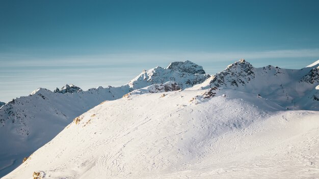 Plano general de montañas cubiertas de nieve bajo un cielo azul claro con media luna