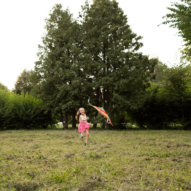 Plano general de niña feliz divirtiéndose con una cometa