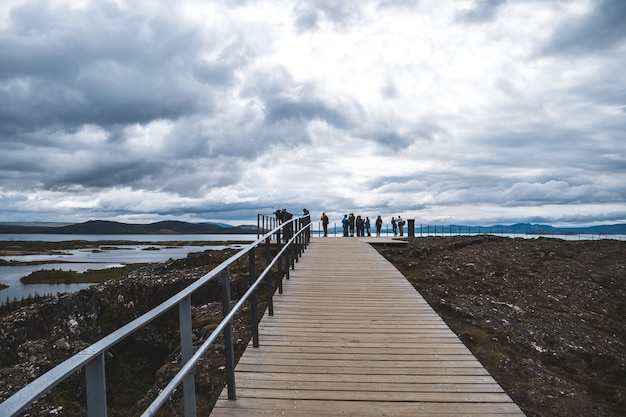 Foto gratuita plano general de un paseo marítimo con barandilla y turistas, con vistas a un lago en un día nublado