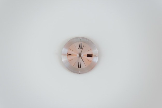 Plano general de un reloj de pared de oro rosa en una pared blanca