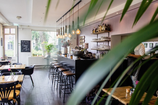 Plano interior de un café con sillas cerca del bar con mesas de madera.