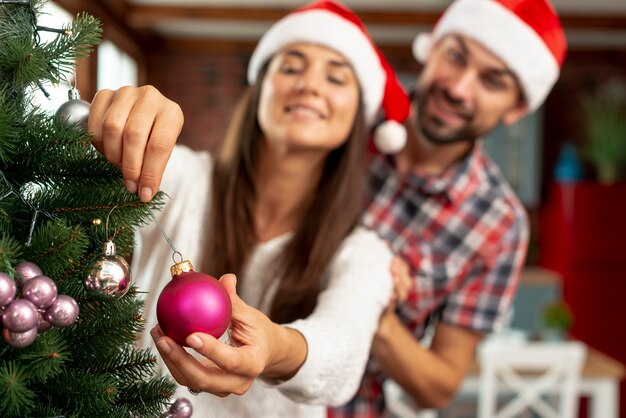 Plano medio borrosa pareja decorando el árbol de navidad