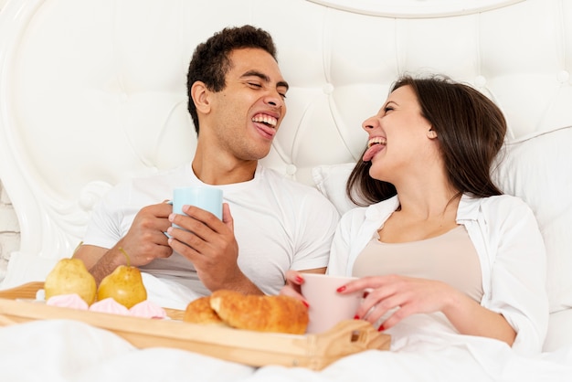 Plano medio divertida pareja desayunando en la cama