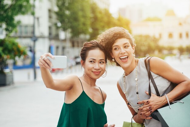 Plano medio de dos amigos tomando selfie al aire libre