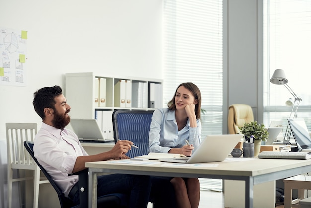 Plano medio de dos compañeros de trabajo sentados en el escritorio y conversando