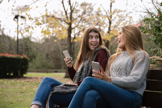 Plano medio de dos mujeres hablando en el parque con teléfonos.