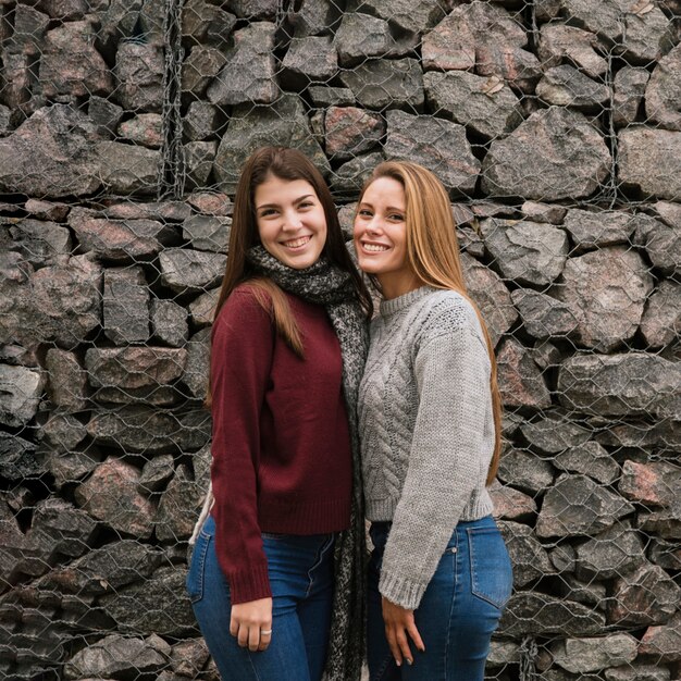 Plano medio de dos mujeres sonrientes frente a un muro de piedra