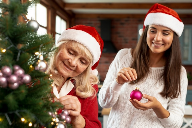 Plano medio feliz madre e hija decorando el árbol de navidad