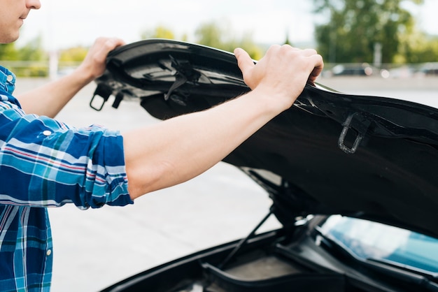 Plano medio del hombre abriendo el capó del automóvil