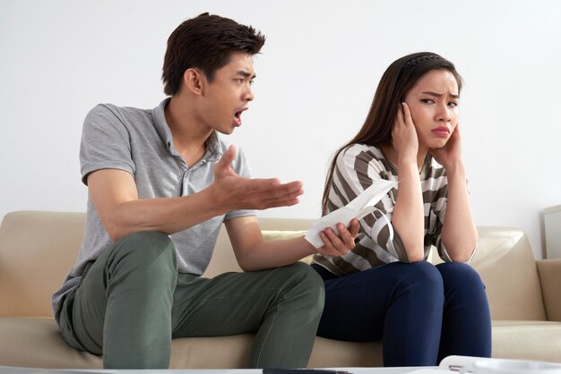 Plano medio del hombre asiático gritando a su esposa sosteniendo un trozo de papel