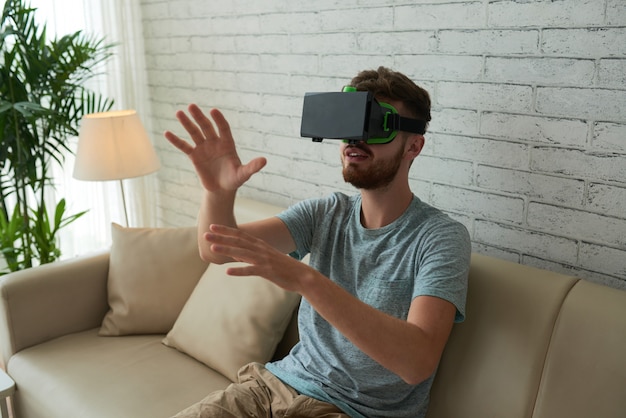 Plano medio del hombre jugando un juego de realidad virtual en el sofá de casa