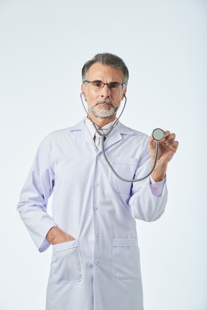 Plano medio del médico mirando a la cámara y gesticulando con el estetoscopio como si estuviera comprobando los latidos del corazón