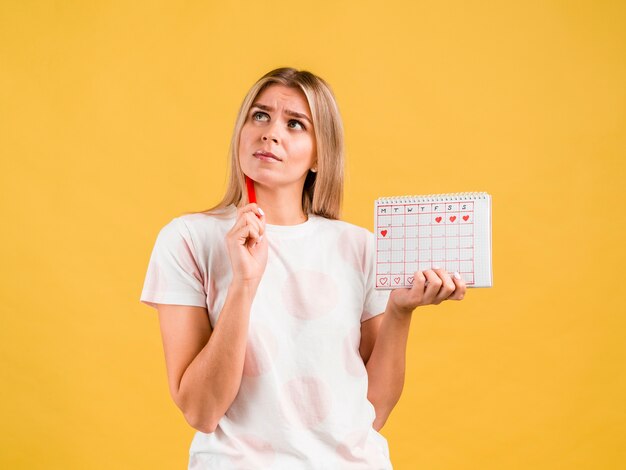 Plano medio de mujer pensando y sosteniendo el calendario del período