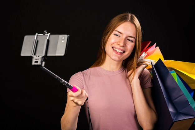 Plano medio de una mujer tomando una selfie con sus bolsas de compras