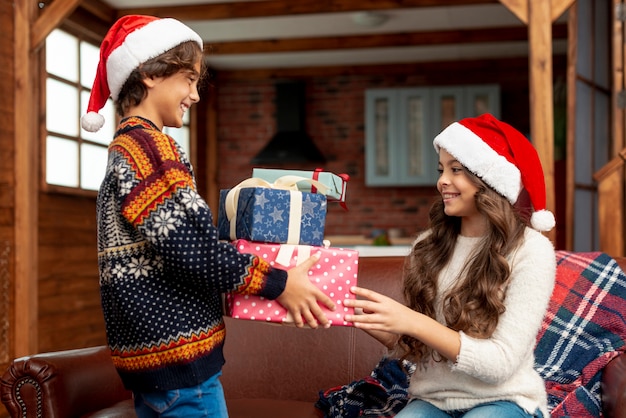 Plano medio, niña y niño felices compartiendo regalos