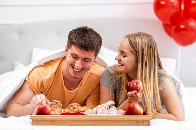 Plano medio pareja feliz comiendo en la cama