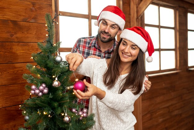 Plano medio pareja feliz decorando el árbol de navidad