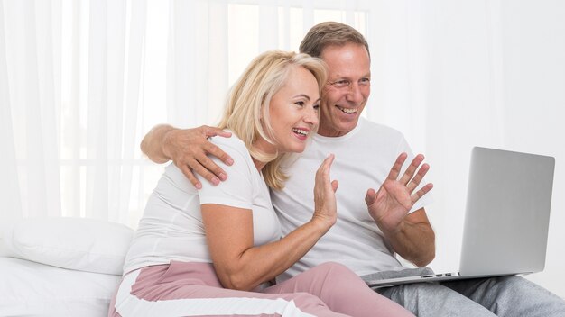 Plano medio pareja feliz con portátil saludando