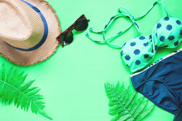 Plano de la puesta de bikini y accesorios con hojas de helecho sobre fondo verde, concepto de verano