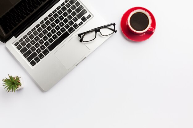 Planta de cactus, taza de café y lentes en la computadora portátil sobre fondo blanco