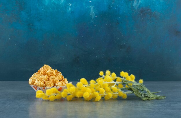 Planta de mimosa por un pequeño montón de palomitas de maíz con sabor a caramelo sobre fondo azul. Foto de alta calidad