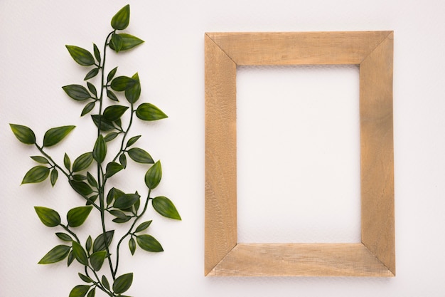 Foto gratuita una planta verde artificial cerca del marco de madera sobre fondo blanco.