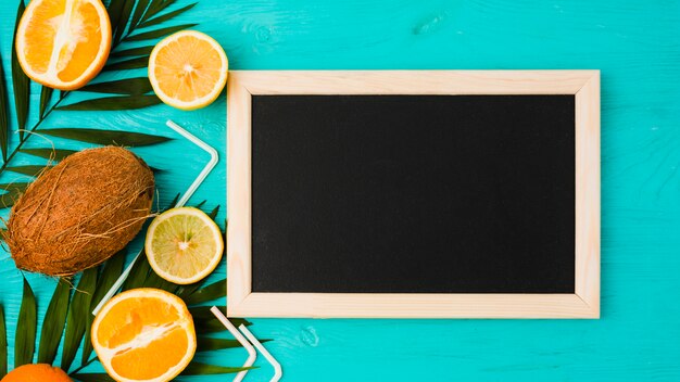 Foto gratuita plantar hojas con frutas y pajitas cerca de pizarra.