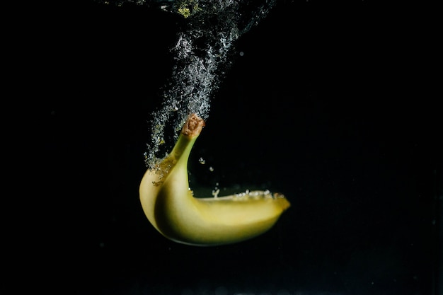 Plátano amarillo cae en el agua y burbujas alrededor de él