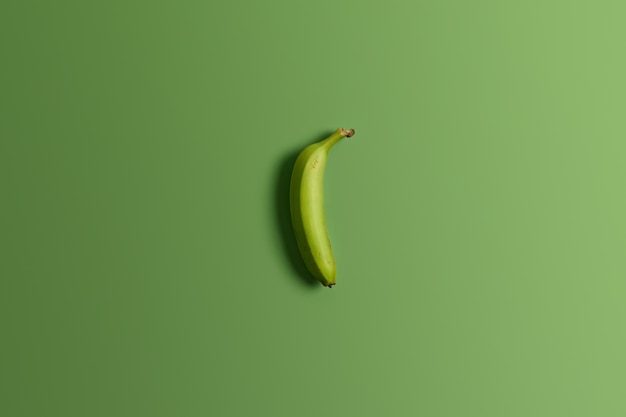 Foto gratuita plátano entero verde inmaduro sobre fondo brillante de estudio. fruta tropical sabrosa y apetecible. comida limpia, merienda saludable, nutritiva y dietética. vista superior y endecha plana. disparo horizontal. concepto de comida