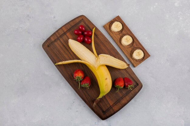 Plátano, fresa y bayas en una bandeja de madera en el medio