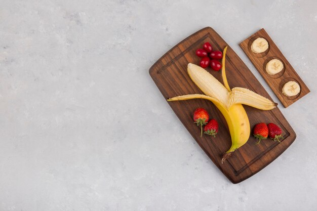 Plátano, fresa y bayas en una bandeja de madera, vista superior