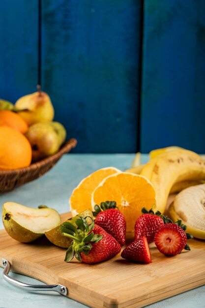 Plátano fresco, naranja y fresas en un tablero azul