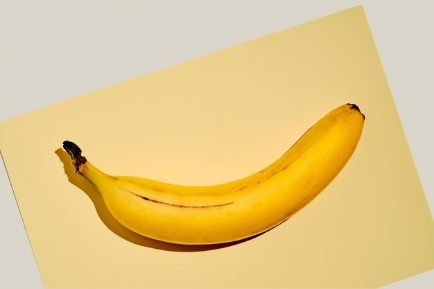 Plátano maduro amarillo sobre una hoja de papel amarillo brillante sobre un fondo gris claro. Idea de fondo de frutas. cosas simples de la vida