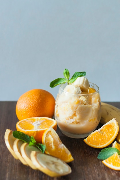 Plátano; naranja entera Menta y helado en vidrio en mesa de madera sobre fondo azul