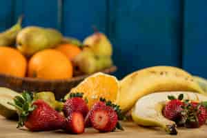 Foto gratuita plátano, pera en rodajas, fresas y naranjas en una pared azul