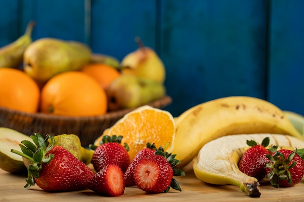Plátano, pera en rodajas, fresas y naranjas en una pared azul